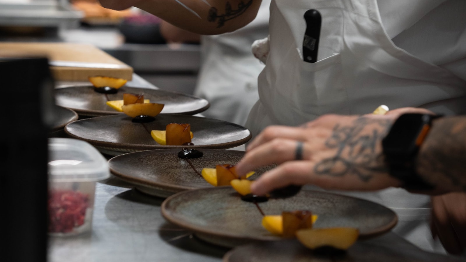 A line cook plating a dish on the hot line during dinner service in a busy restaurant kitchen